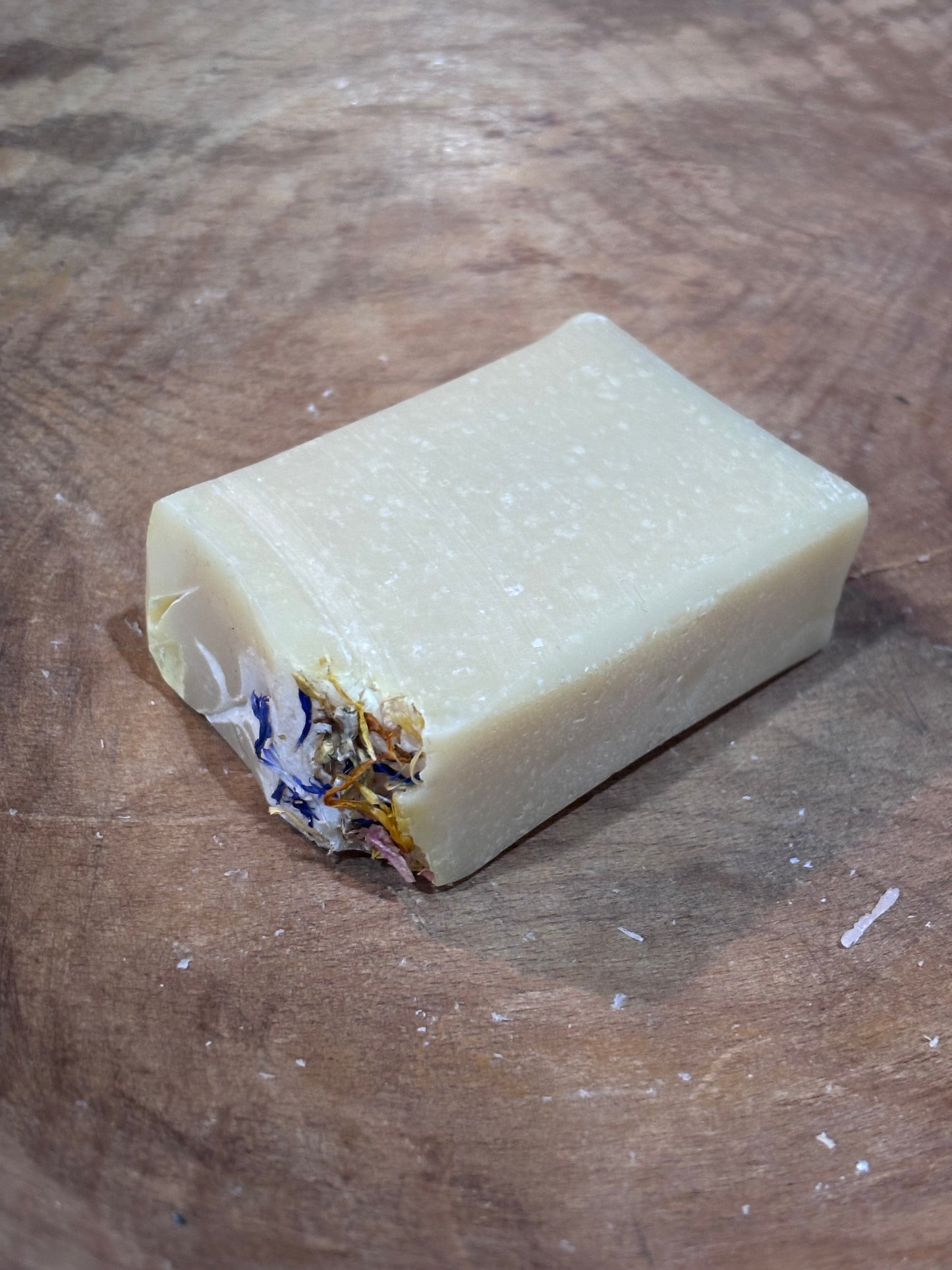 Blue Ridge Wildflower soap. Creamy pale yellow wildflower soap with dried botanical. Ingredients include saponified oils of olive, palm, coconut, and castor, fragrance oils, and dried botanicals.