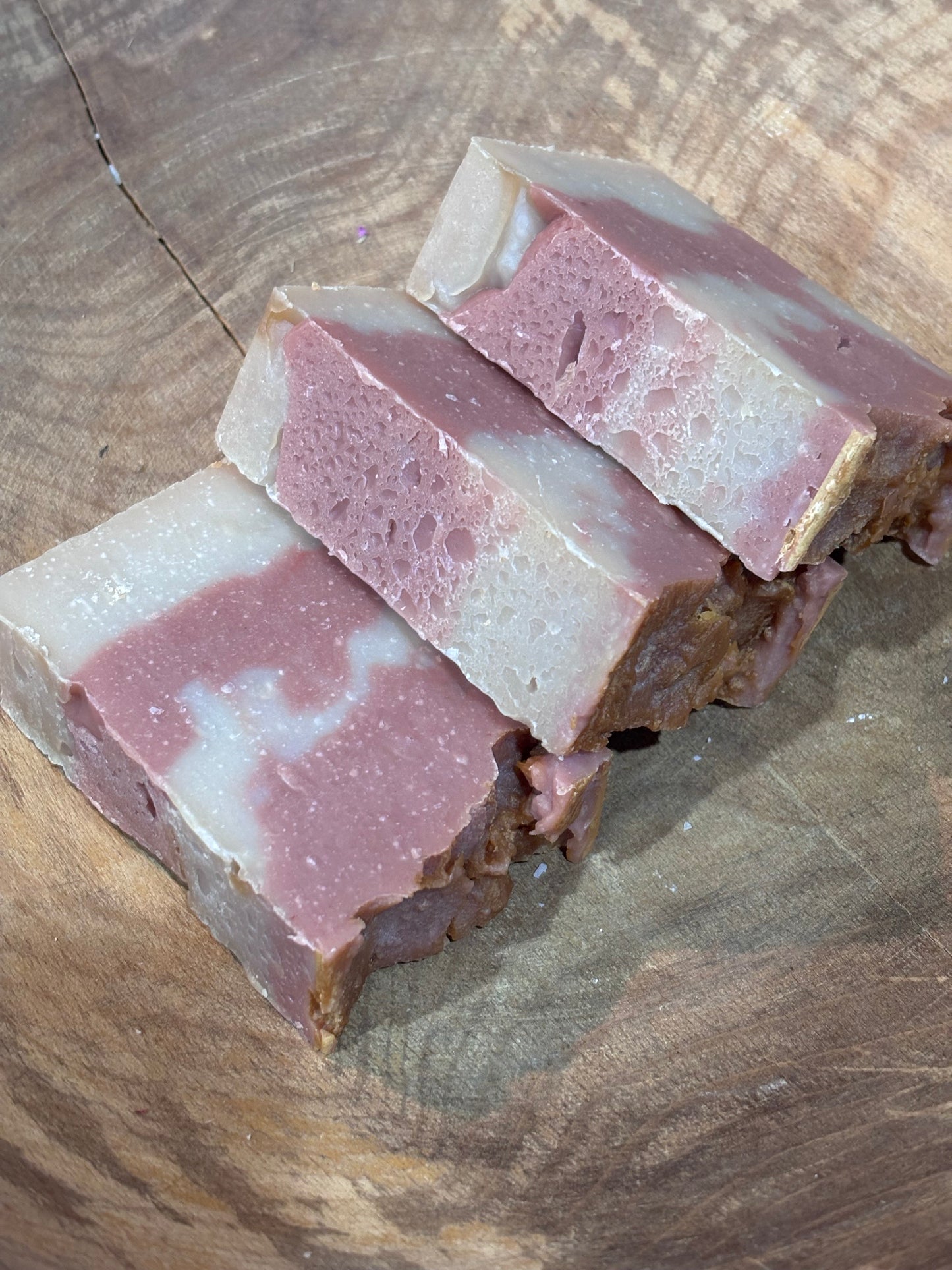 3 bars of pink and cream colored soap laying in a wooden bowl.

Ingredients include  saponified oils of olive, palm, coconut, castor, cocoa butter, avocado, fragrance oil and rose clay.
