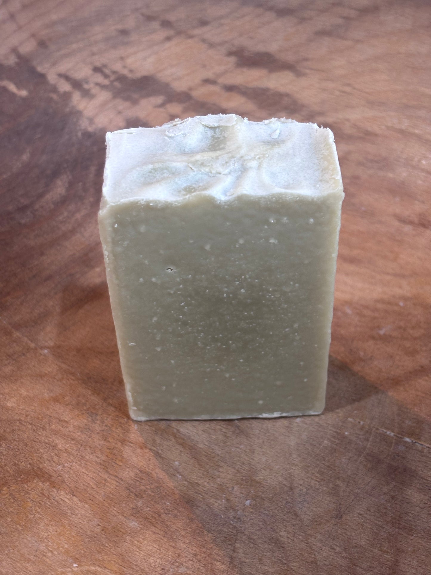 Light green soap in a wooden bowl. Ingredients: distilled water, saponified oils of olive, palm, coconut, castor, patchouli essential oil and fragrance oil blend, sea clay