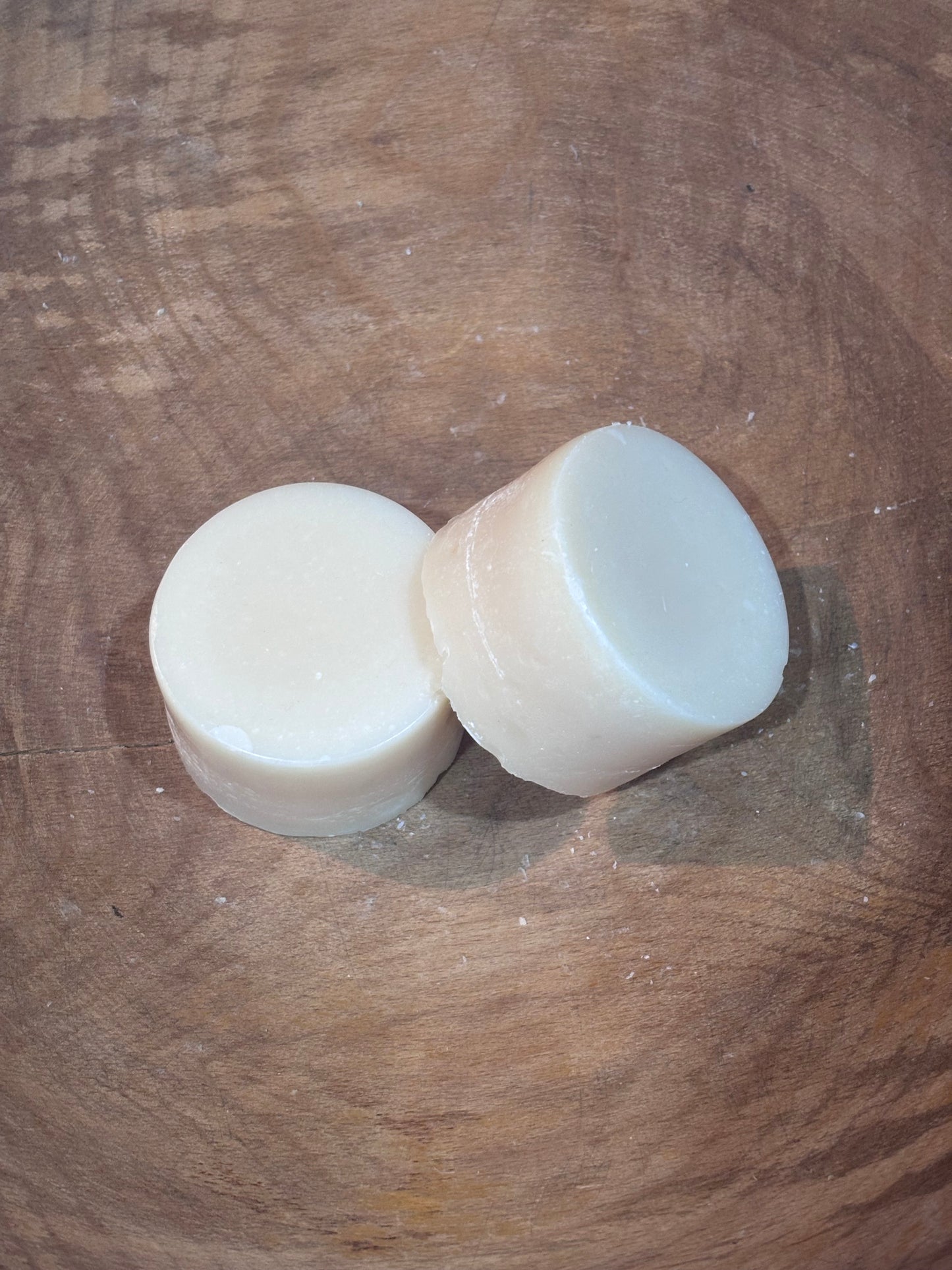 Two round dish soaps laying on a wooden bowl. Ingredients include distilled water and saponified oils of coconut, castor and spearmint and lavender essential oils