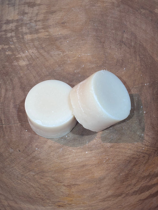 Two round dish soaps laying on a wooden bowl. Ingredients include distilled water and saponified oils of coconut, castor and spearmint and lavender essential oils