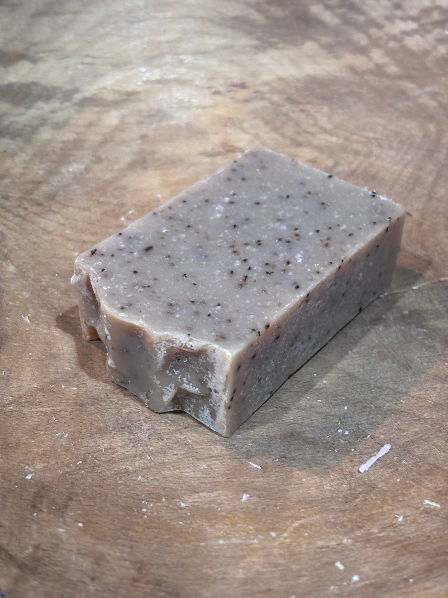 Pumpkin Sandalwood soap. It is beige soap with coffee grounds laying in a wooden bowl. Ingredients include saponified oils of olive, palm, coconut, castor, cocoa butter, avocado oil, fragrance oils and ground coffee.  